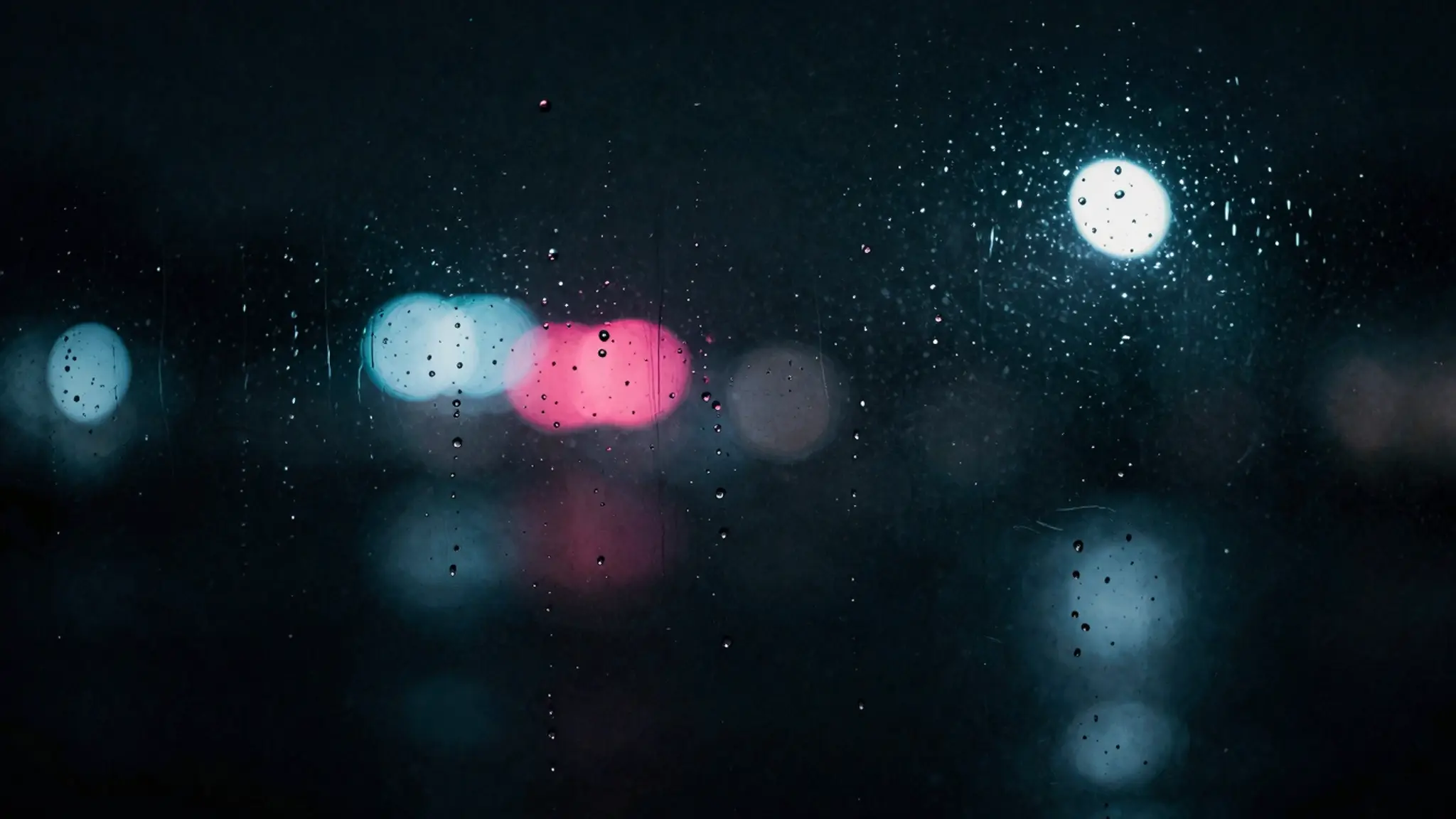 White, blue and pink lights glowing through a rain-covered window