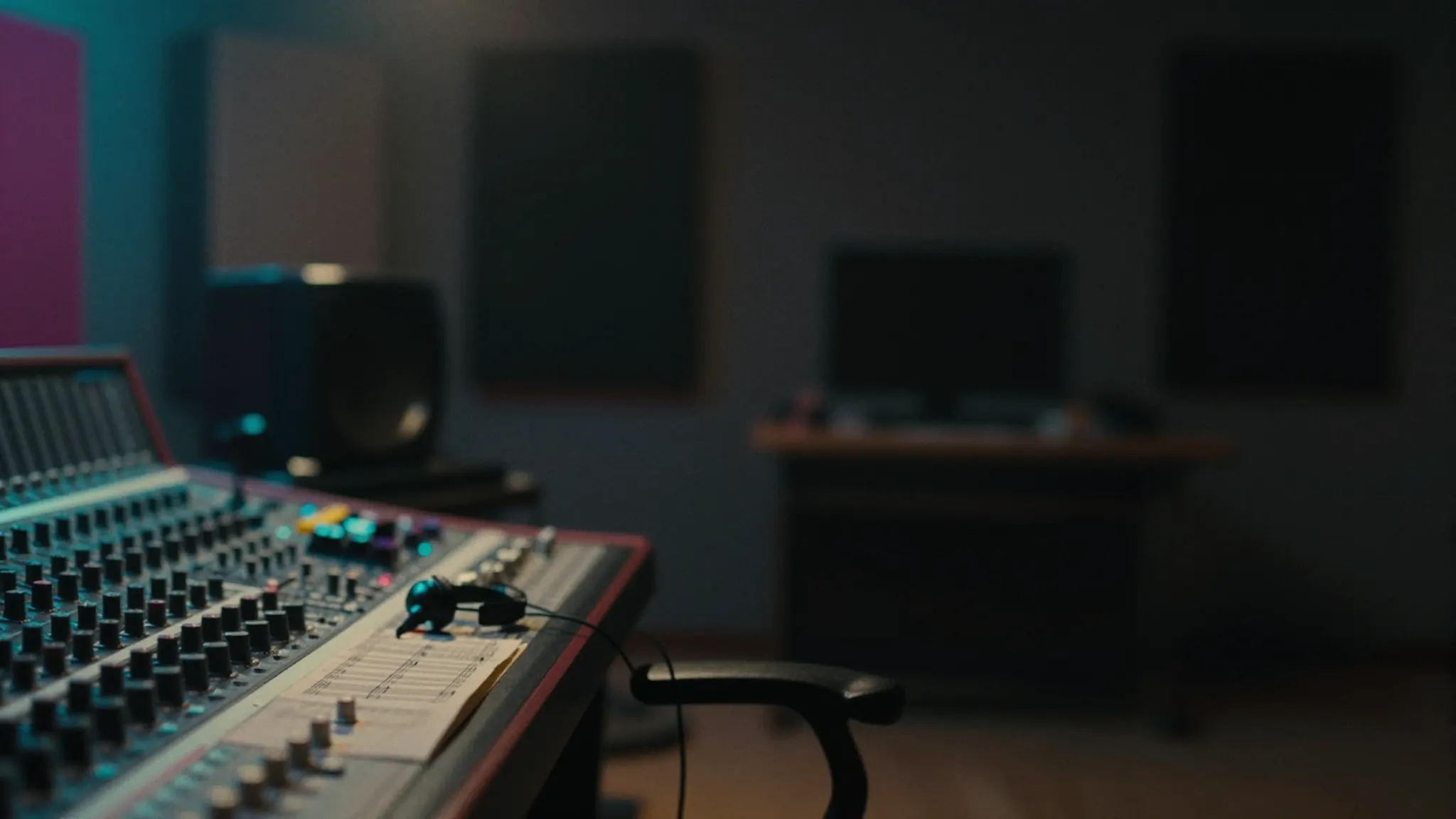 Darkened home recording studio lit by teal and magenta light, with a mixing desk silhouetted at the left of the frame