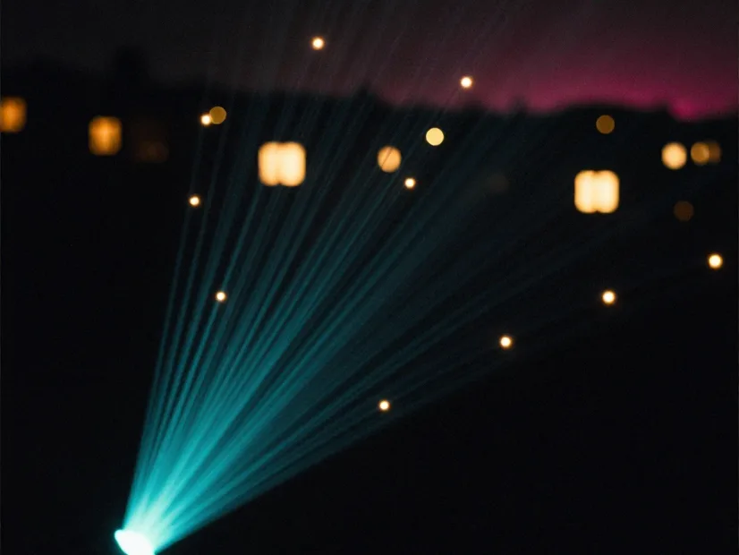 A single beam of teal light fanning out across a dark valley towards many separate lit windows.